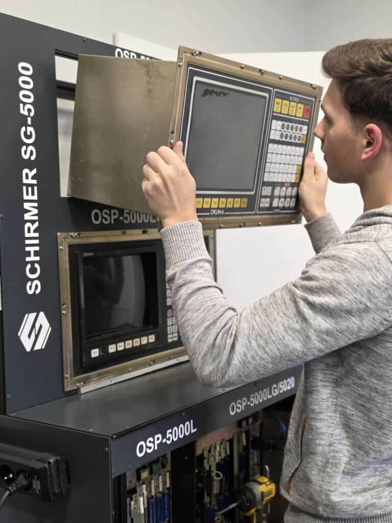 Technician testing and inspecting an Okuma OSP control panel on the SCHIRMER SG-5000 test stand