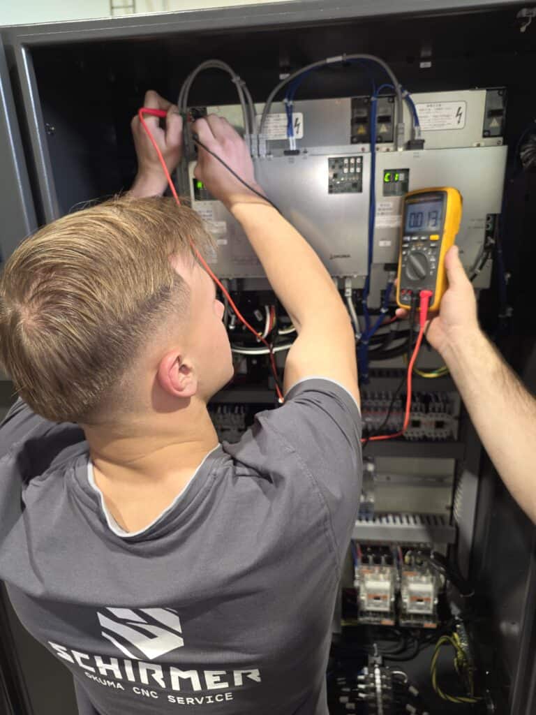 Technician performing Okuma CNC electronics repair and diagnostics inside control cabinet