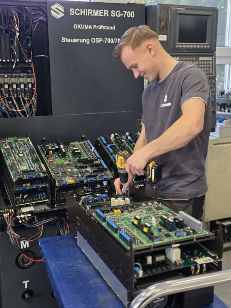 Técnico reparando módulos electrónicos de CNC Okuma en el banco de pruebas SG-700 de Schirmer GmbH.